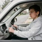 Jeune adolescent de 14 ans assis au volant d'une voiture sans permis électrique dans un quartier résidentiel