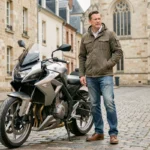 Homme debout à côté d'une moto moderne sur une rue pavée de Poitiers avec des bâtiments historiques en arrière-plan