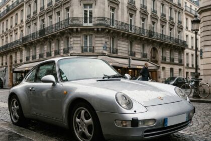 Porsche 911 argentée garée dans une rue parisienne, vue en angle avant trois quarts pour illustrer une assurance auto haut de gamme