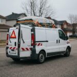 Renault Trafic chargé avec débord de charge sécurisé par des sangles orange et signalé par un triangle rouge visible à l'arrière du véhicule