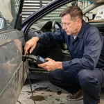 Technicien automobile connectant un scanner OBD-II pour vérifier l'électronique moteur numérique d'une voiture d'occasion en atelier