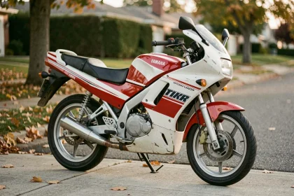 Yamaha TZR 50cc des années 90 garé dans une rue résidentielle, vue 3/4 avant mettant en valeur le carénage sportif et la livrée blanc et rouge